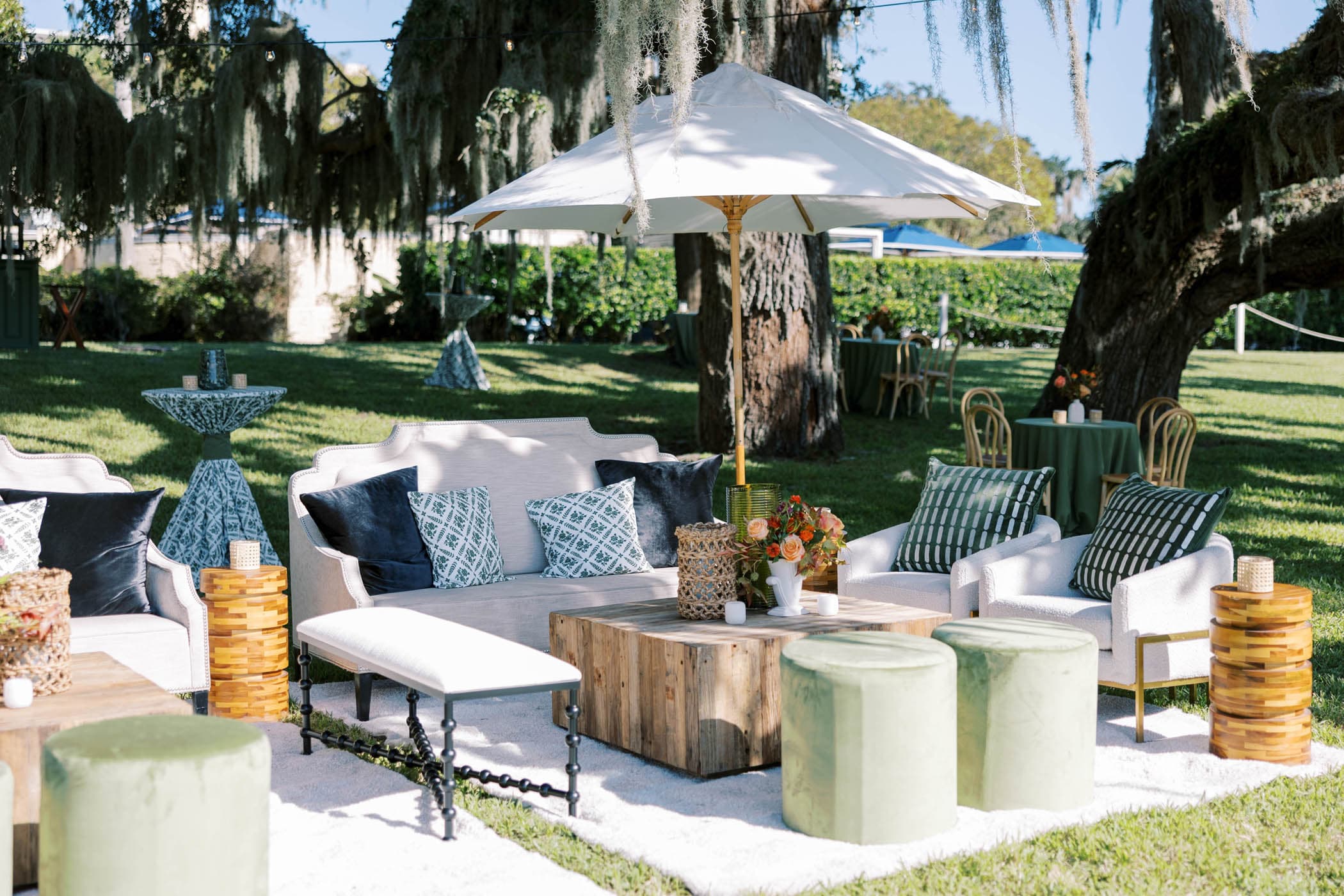 A private outdoor lounge area for a group with comfy couches and chairs, umbrellas to block the sun and a beautiful green space