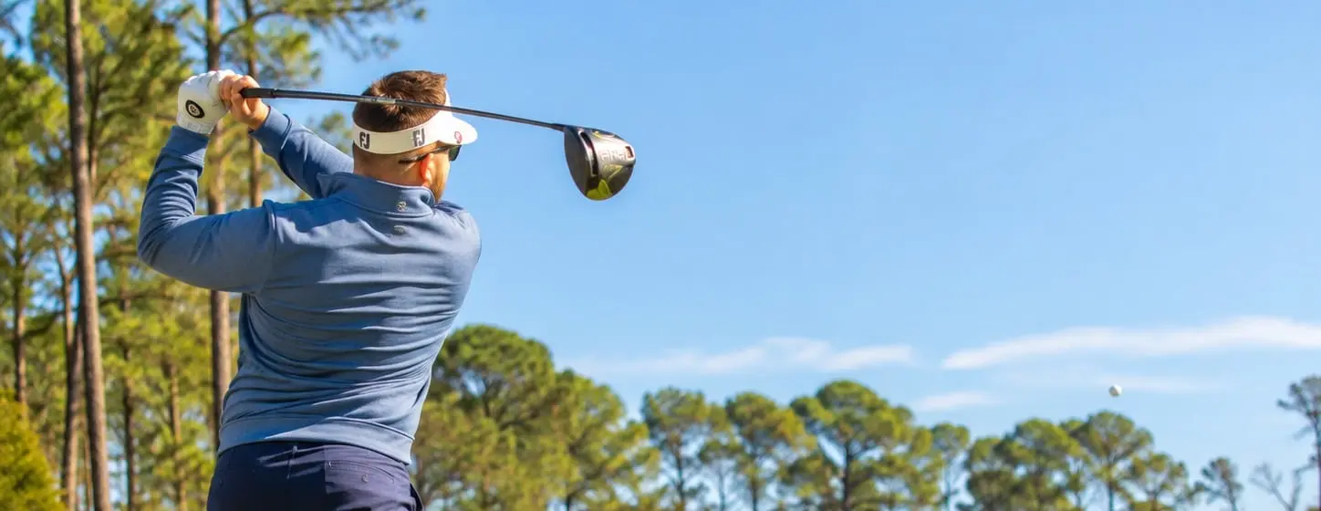 Golfer driving a tee shot down a sunny fairway lined with tall pines on the championship golf course at Jekyll Island Club Resort in Georgia.