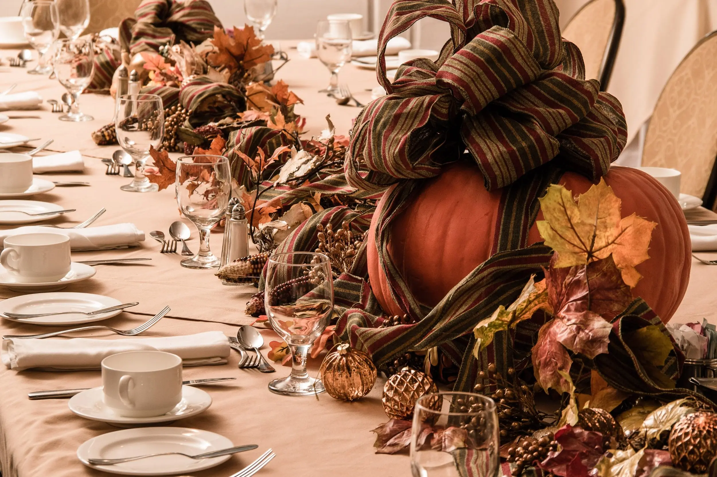 Elegant Thanksgiving banquet table at Jekyll Island Club Resort in Georgia, set with fine china and stemware and finished with a pumpkin centerpiece, autumn leaves and a striped ribbon garland.